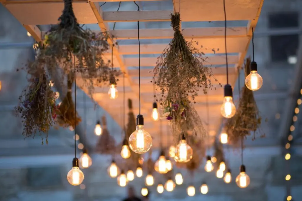 Warm glowing light bulbs hanging from a wooden frame, paired with dried floral arrangements, creating a rustic and cosy atmosphere for a wedding reception.