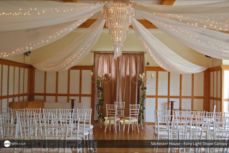 chandelier with fairy lit drapes over a wedding venue with chairs